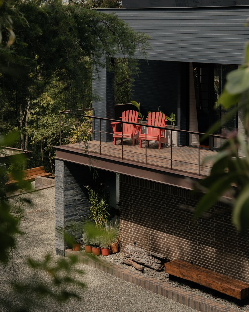 Cantilevered timber deck with wire railing and red chairs overlooking a planted courtyard