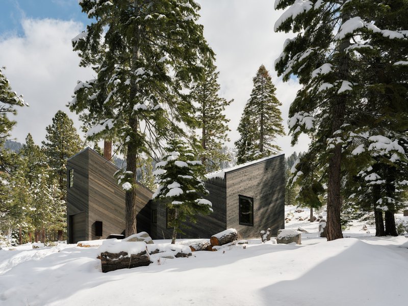 Facade of interlocking wood clad volumes framed by snow covered conifers and boulders