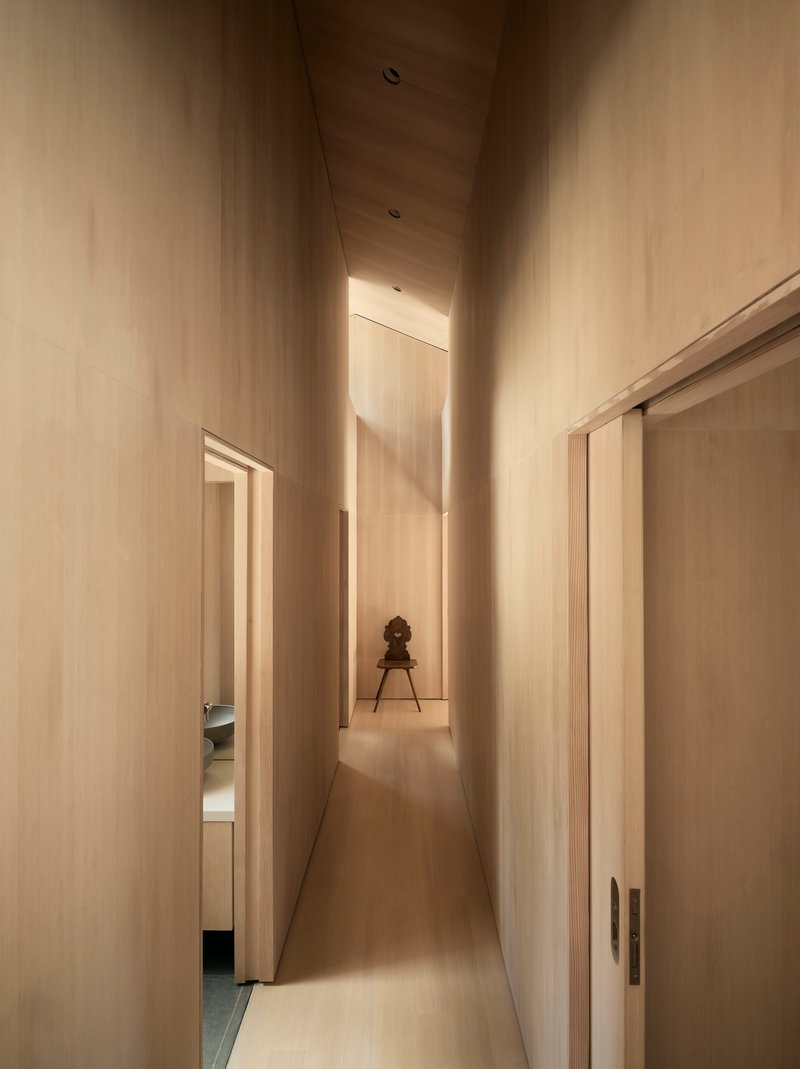 Narrow corridor with light wood walls and ceiling framing a small chair at the end