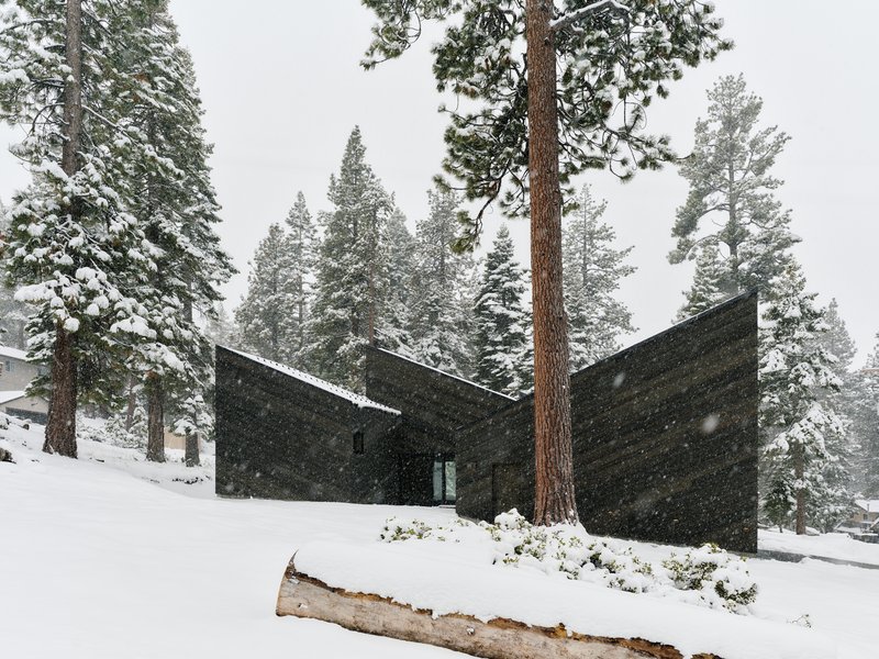 Angled timber-clad forms meeting at sharp corners during active snowfall among forest pines