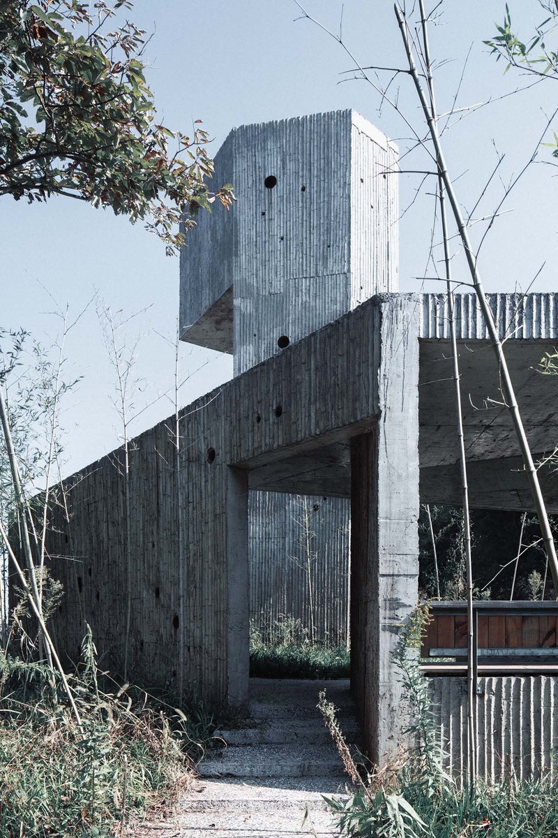 Covered entry passage beneath cantilevered concrete volumes with board-formed surfaces and circular openings