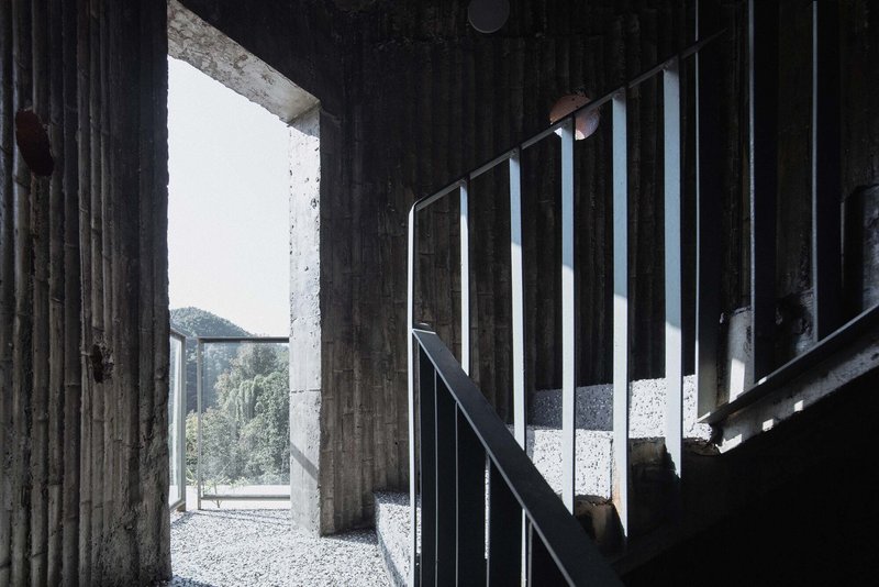 Interior staircase with steel railings framed by board-formed concrete walls and gravel floor