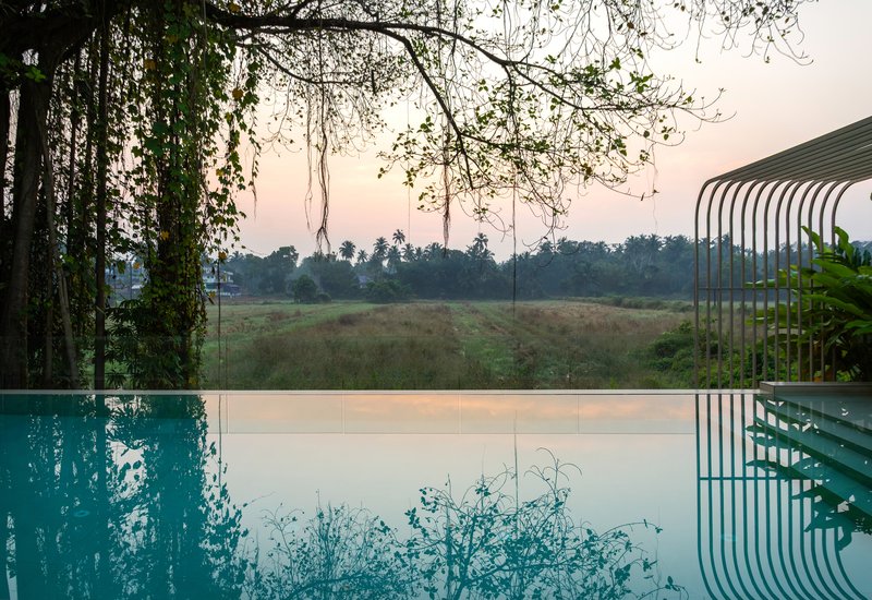 Infinity pool edge with curved metal canopy overlooking fields at dusk