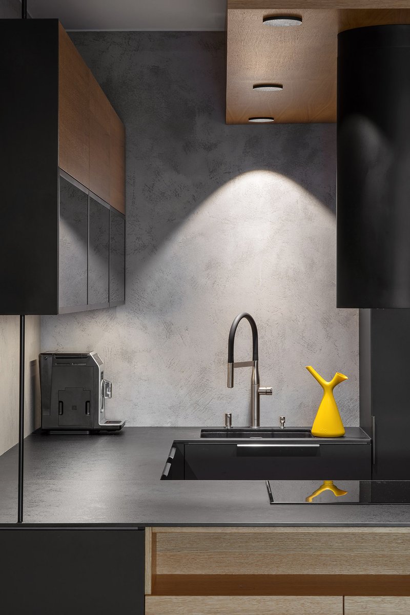 Minimal black kitchen with oak detailing and a bold mustard accent