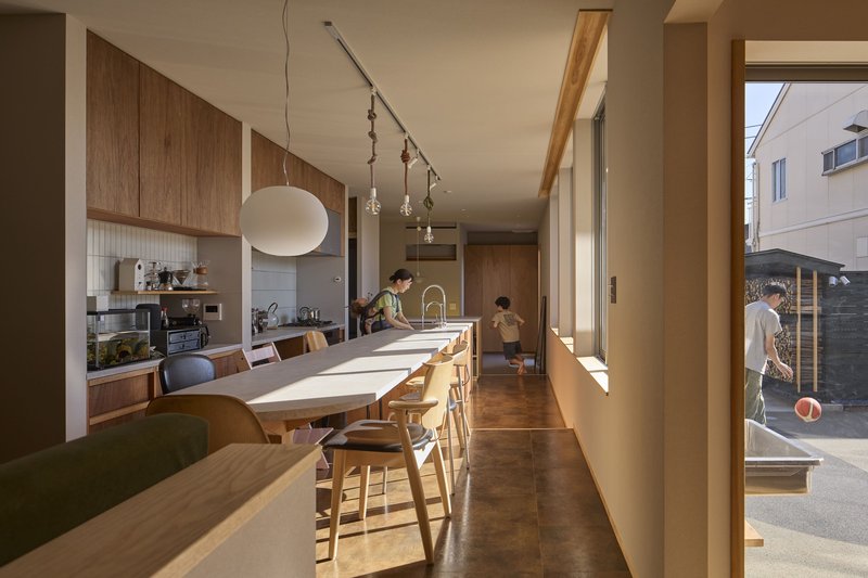 Kitchen and dining area with timber cabinetry and a long table flooded with afternoon sunlight