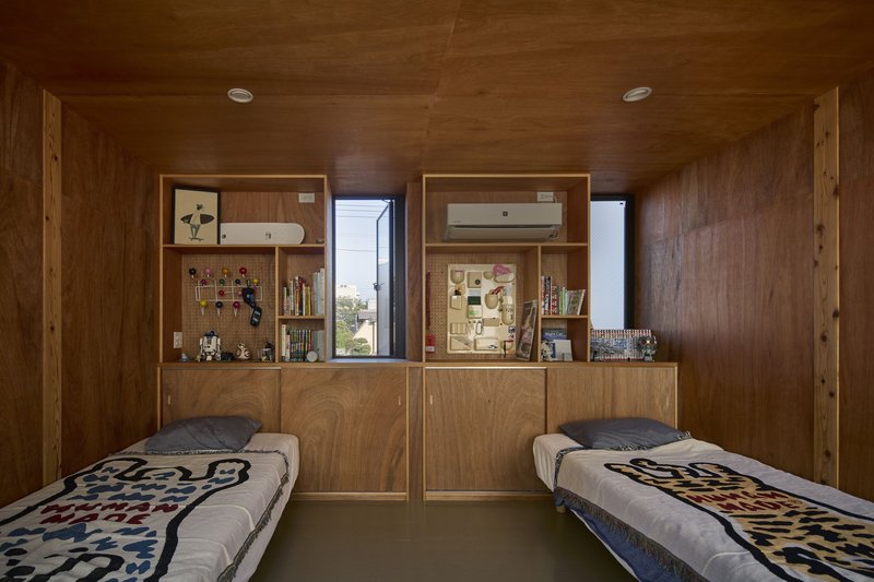 Twin beds in a wood-clad room with built-in storage and narrow windows framing views to neighboring rooftops