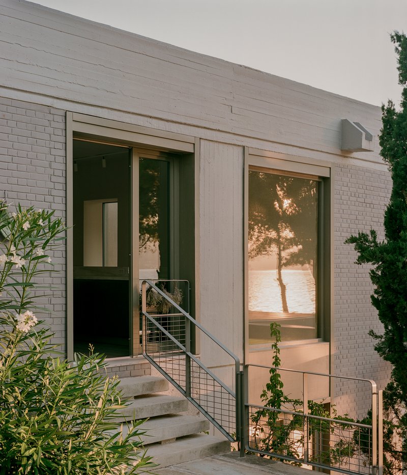 Entry with wire mesh balustrade and concrete steps against white brick wall at sunset