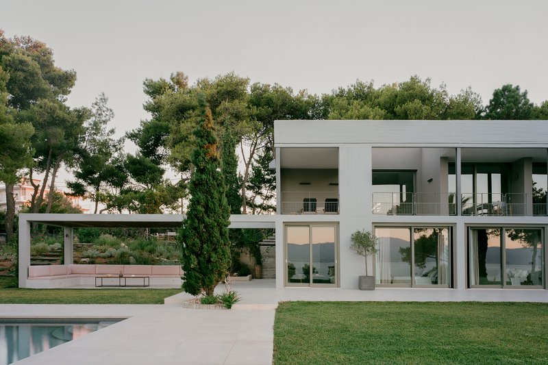 White concrete and glass facade with two-story glazing overlooking a lawn and pool under overcast skies