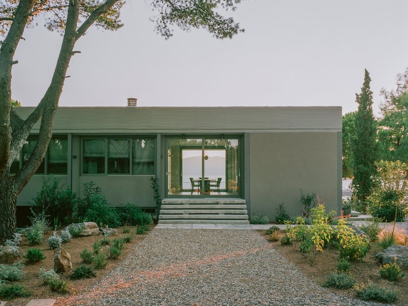 Entry facade with gravel driveway, planted beds, and concrete steps leading through glazed sliding doors