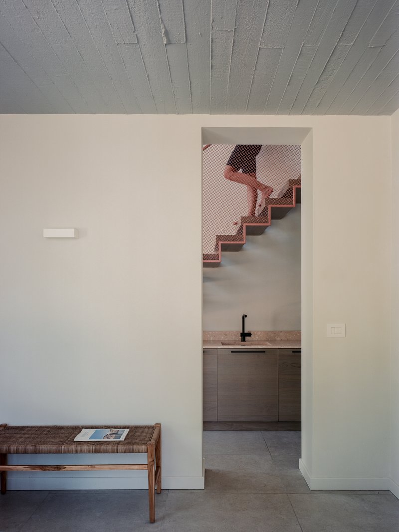 Doorway through a white wall revealing a copper mesh staircase rising beyond a kitchen counter