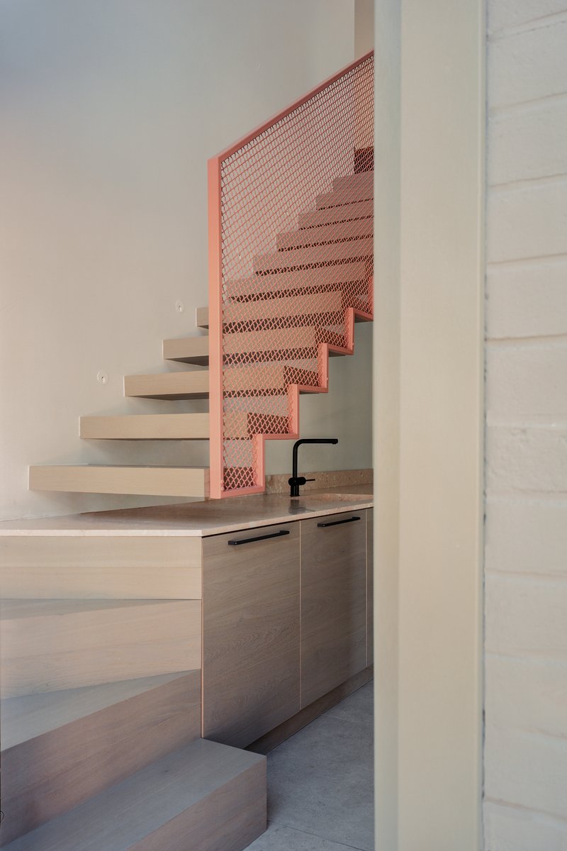 Helical staircase with pale stone treads and copper expanded metal balustrade beside a sink counter