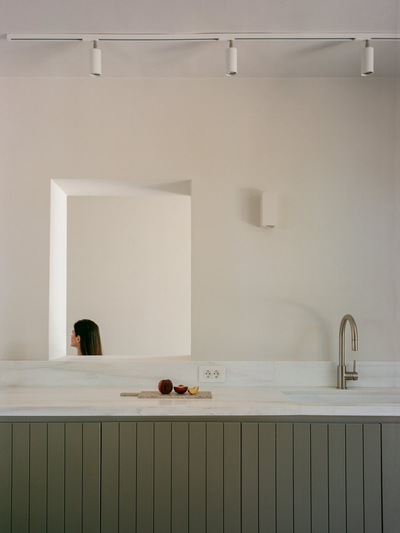 Kitchen counter in pale marble with vertical tongue-and-groove cabinetry and a framed wall mirror