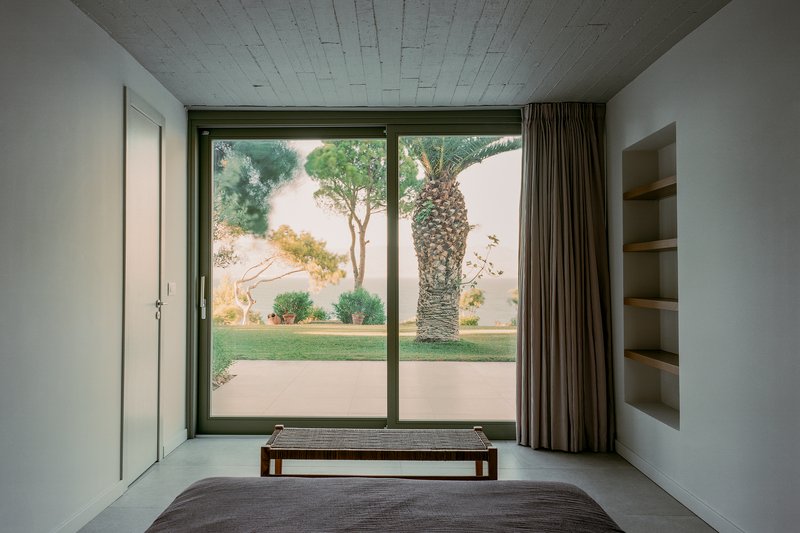 Bedroom with full-height glazed door opening to a courtyard with palm tree and lawn