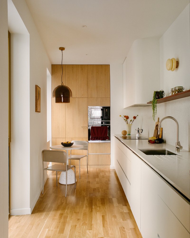Galley kitchen with white counters and timber cabinetry under warm natural light from adjacent spaces