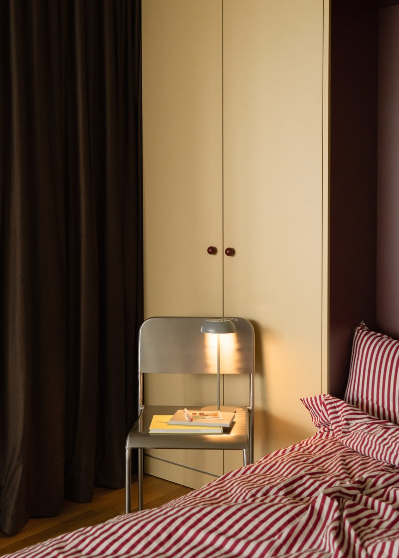 Pale yellow wardrobe with brown knobs beside a bedside table lamp in evening light