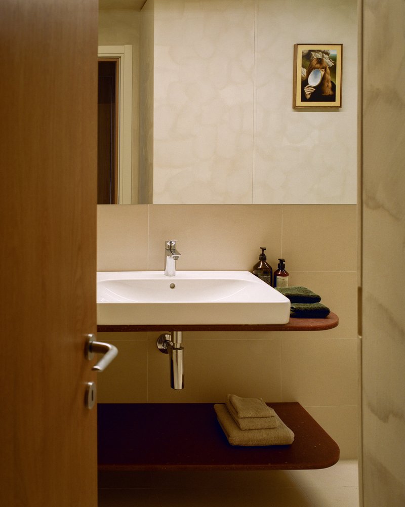 Bathroom vanity with wall-mounted sink and curved timber shelves under reflected doorway