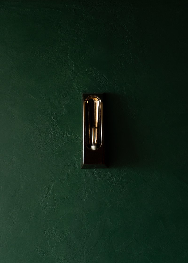 Black wall sconce with exposed filament bulb centered on a deep green plaster wall
