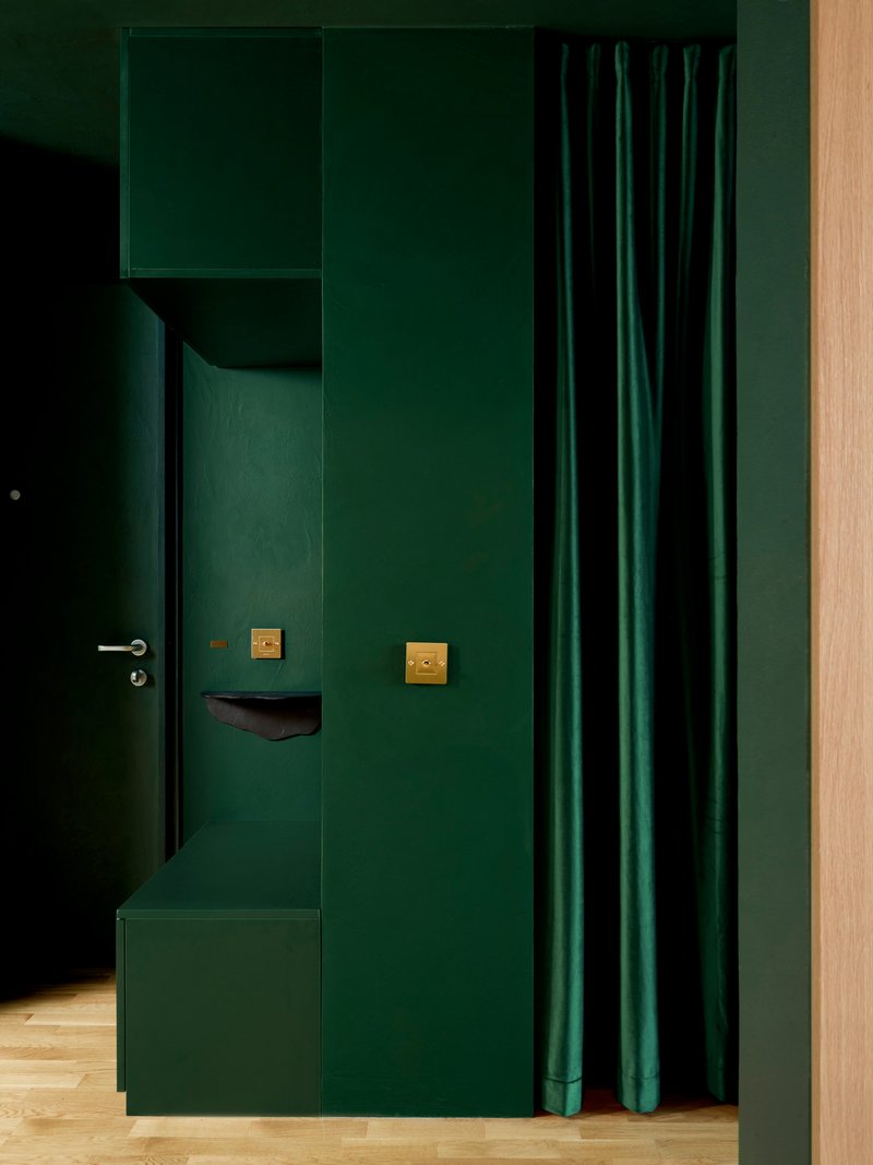 Green entryway volume with wall-mounted coat hooks, brass switches, and curtain beside an oak door frame