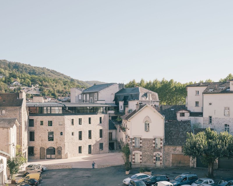 Elevated view of clustered stone buildings with a glazed rooftop addition and hillside beyond
