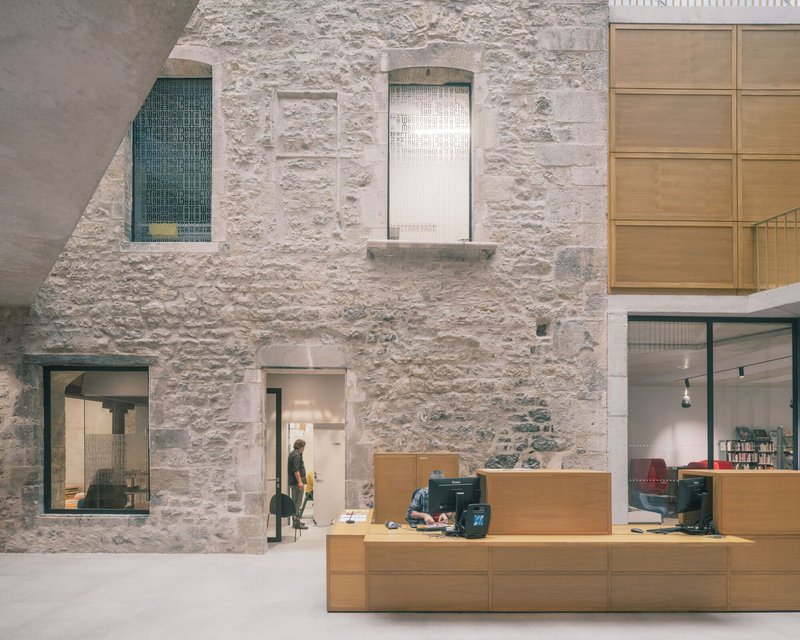 Stone wall with arched openings adjacent to a timber reception desk in a daylit interior
