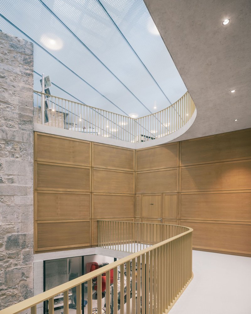 Upward view of curved timber balcony with vertical slats beneath a translucent skylight