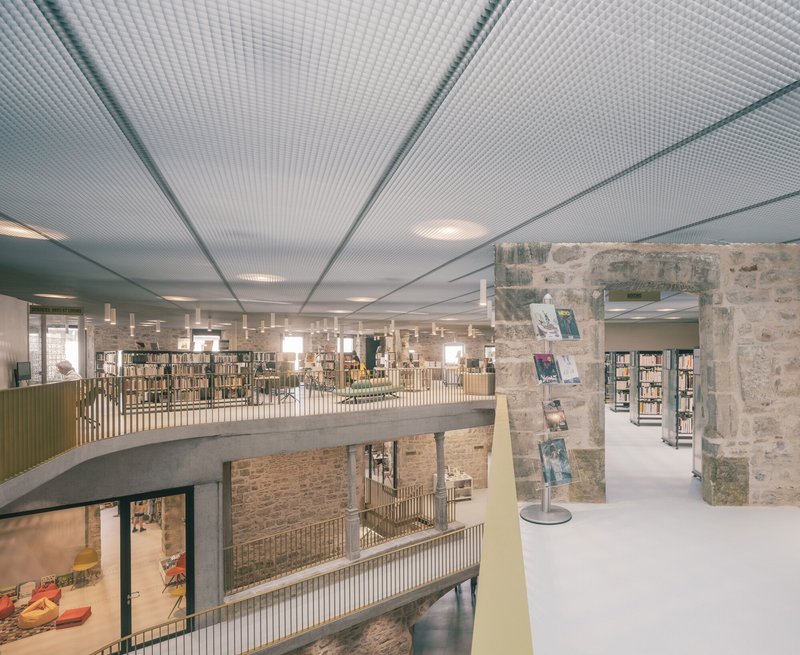 Upper level view showing perforated metal ceiling panels and concrete mezzanine railing overlooking the atrium below