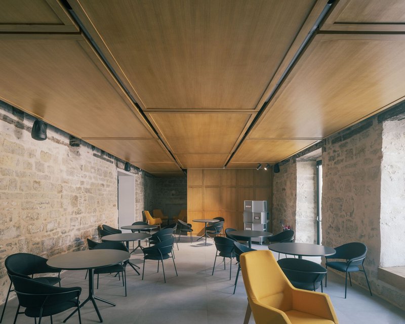 Reading room with exposed stone walls and timber ceiling panels above tables with dark chairs