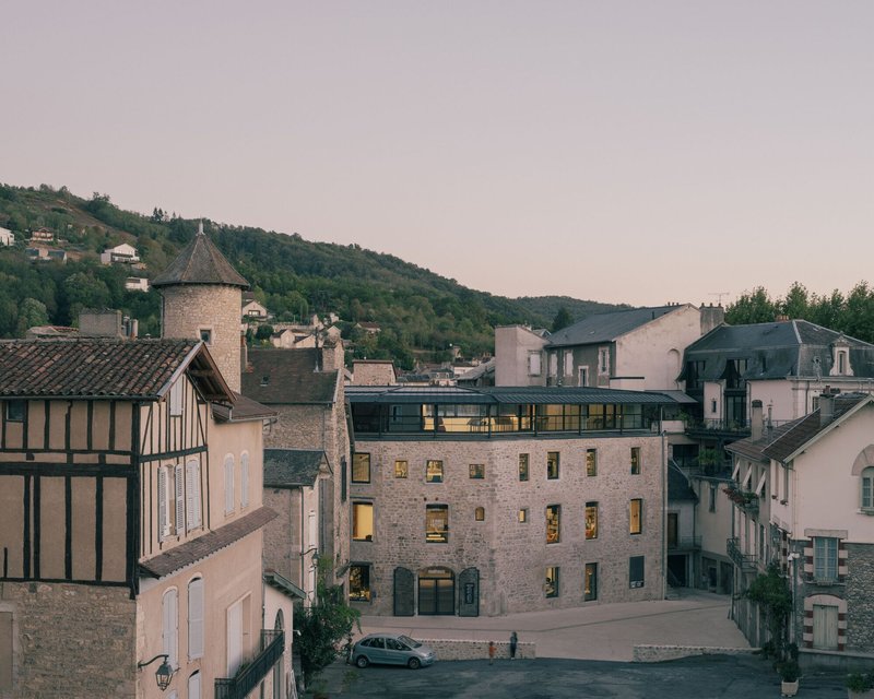 Stone building with illuminated windows nestled among historic village structures at dusk