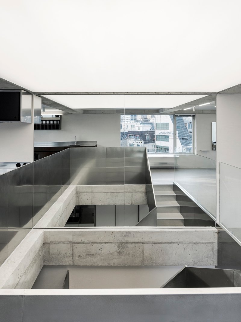 Split-level interior with stainless steel kitchen island and concrete beams crossing over glazed openings