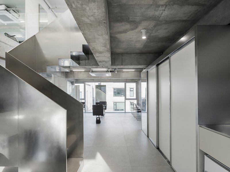 Corridor with exposed concrete ceiling beams, stainless steel partitions, and sliding white panels along the walls