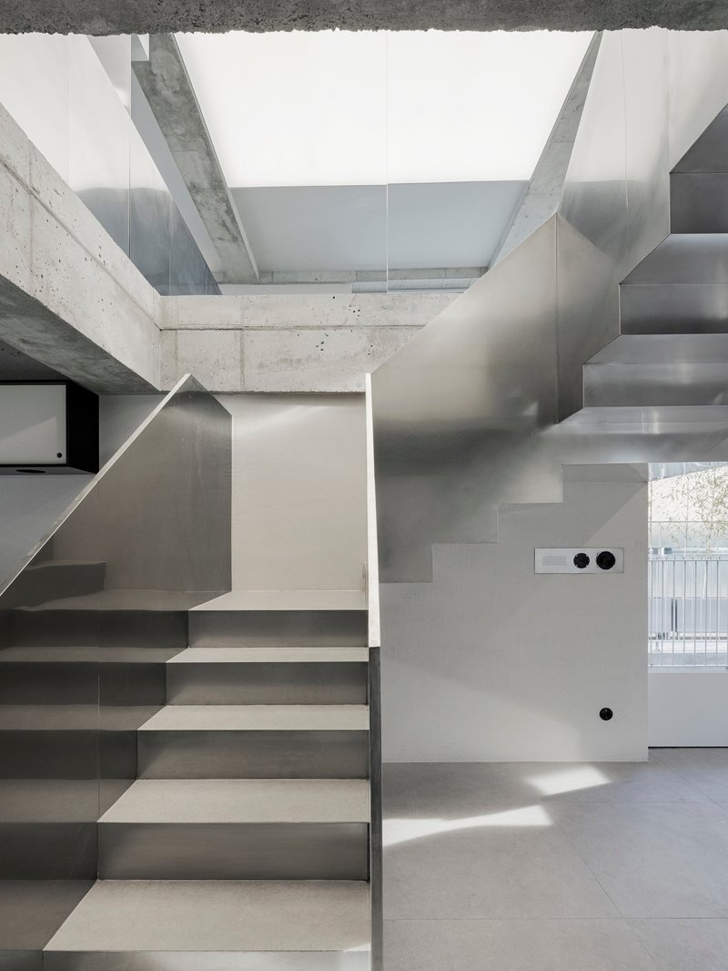 Intersecting stainless steel staircases beneath concrete beams with bright daylight casting sharp shadows