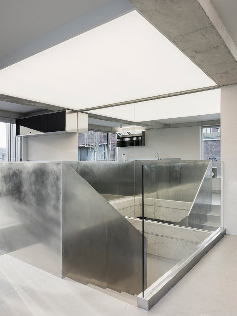 Concrete stairwell enclosed by translucent glass panels and brushed steel walls beneath an exposed ceiling