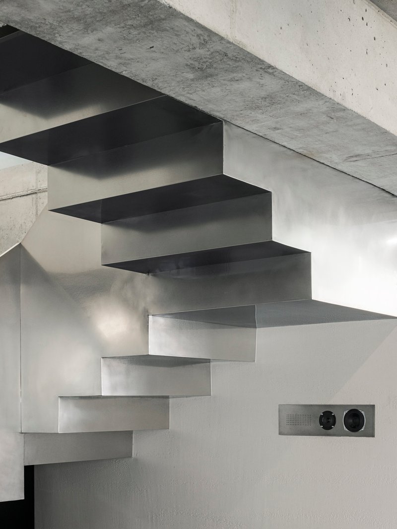 Cantilevered steel staircase with folded treads ascending against a white wall in natural light