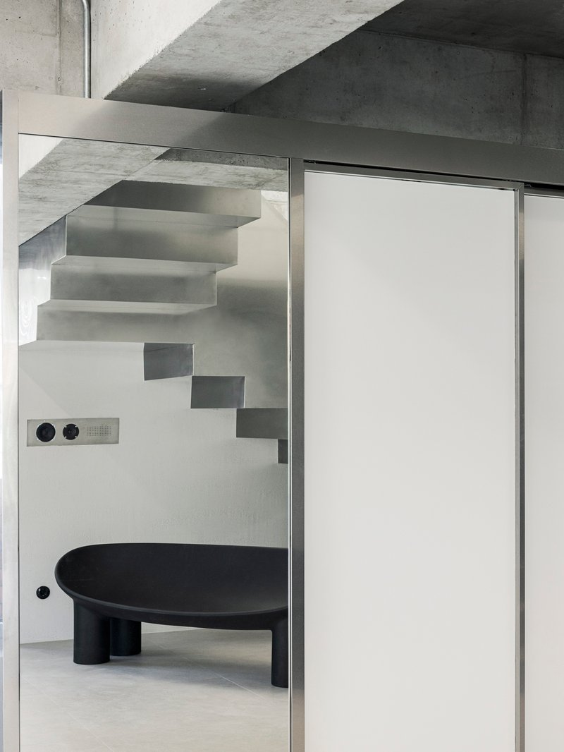 View through glass partition showing floating steel stairs and a black circular table below