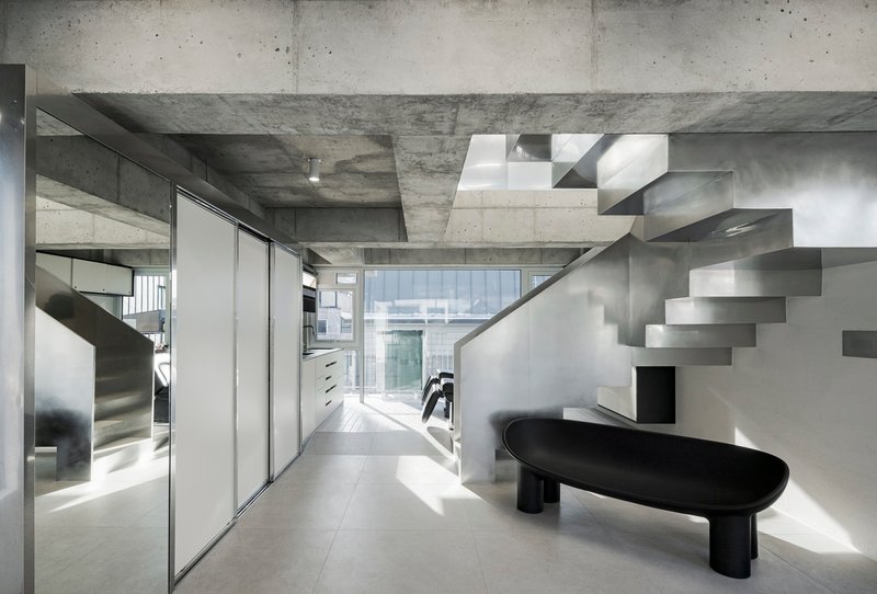 Interior view of the folded steel staircase rising against white walls beneath exposed concrete beams