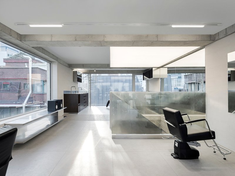 Open salon space with stainless steel partition walls and large windows overlooking neighboring buildings
