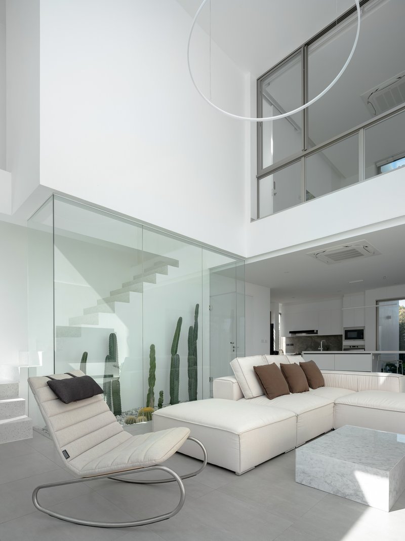 Living space with glass-enclosed staircase, suspended ring light, and tall cacti visible through glass partition