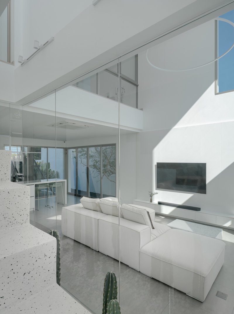 View across polished terrazzo floor through glass wall dividing living area from open kitchen in bright sunlight