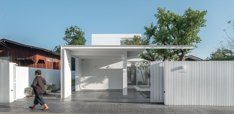 Street facade with white corrugated metal fencing and open carport framing a person walking past