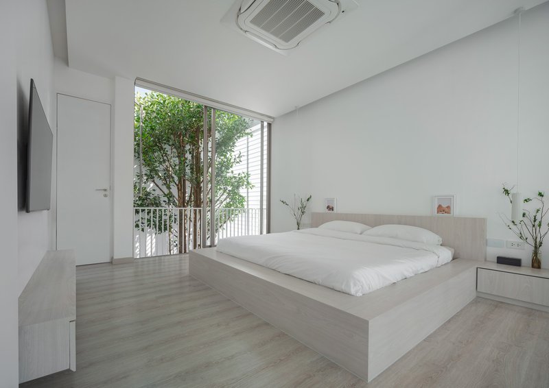 Bedroom with raised platform bed and full-height glazed doors opening to a small tree courtyard