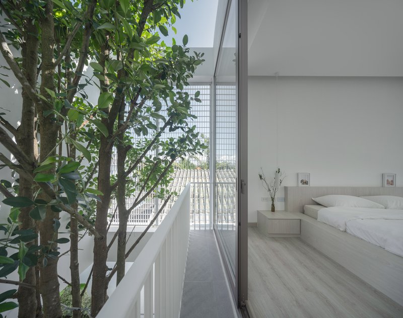 Bedroom opening to a narrow balcony with white vertical railings and trees behind glass block screens