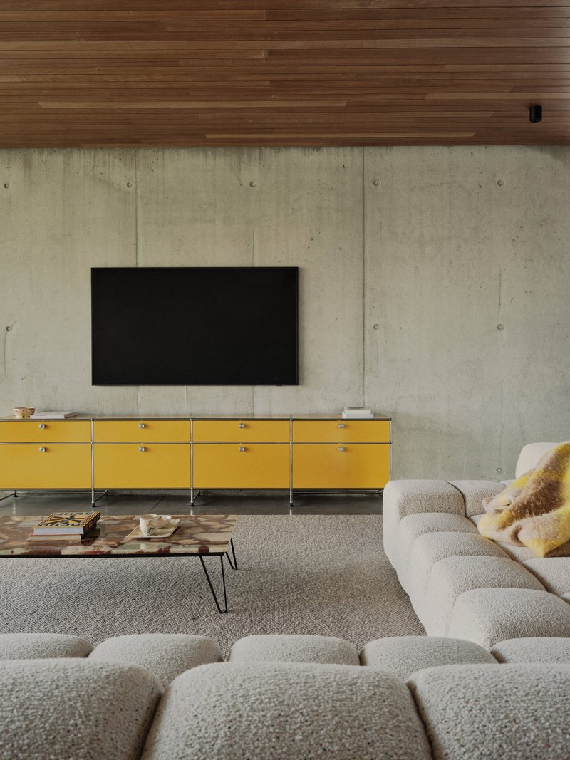 Living room with board-formed concrete wall, timber ceiling and yellow modular credenza beneath flat screen