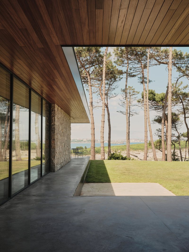 Covered terrace with timber soffit and stone wall opening to lawn and distant water view