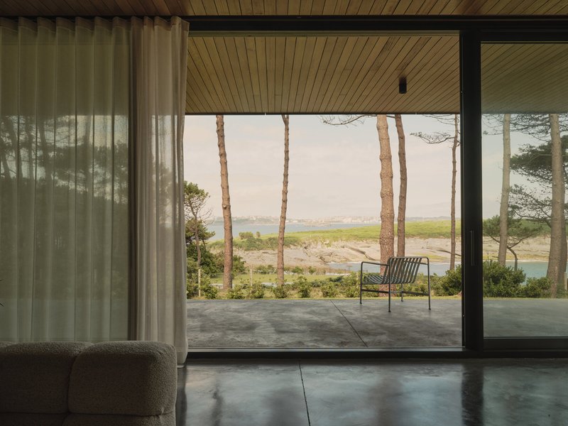 Floor-to-ceiling glazing framing a covered terrace with views of water and pine trees