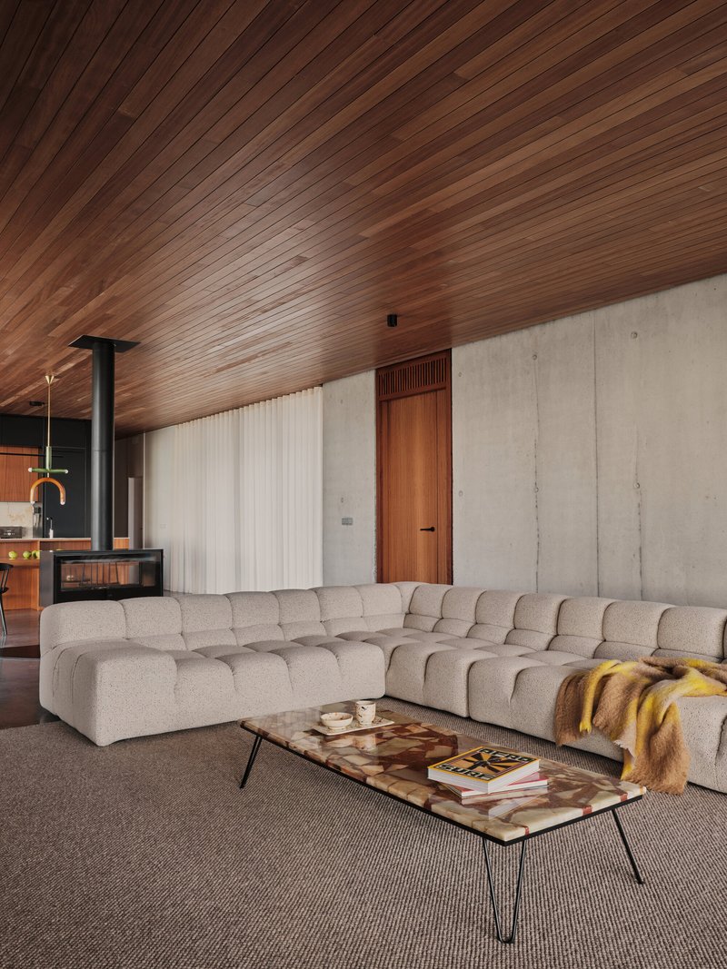 Sectional sofa beside board-formed concrete wall with timber door and sheer drapery