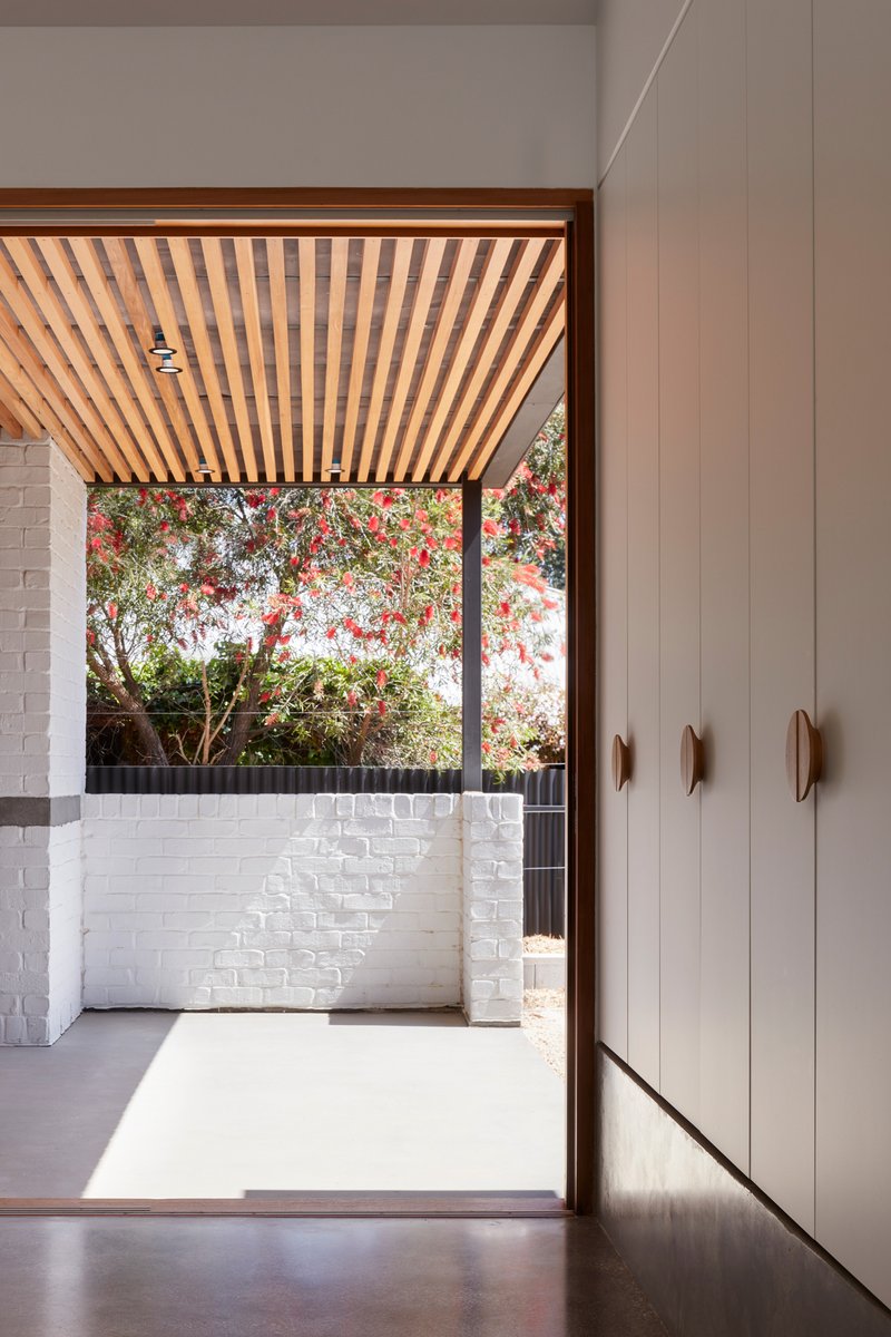 Doorway with timber batten ceiling opening to a white brick courtyard with flowering tree overhead