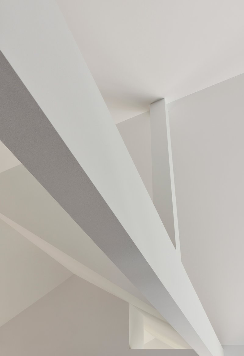 Ceiling detail showing white painted steel beams crossing at angles in soft daylight