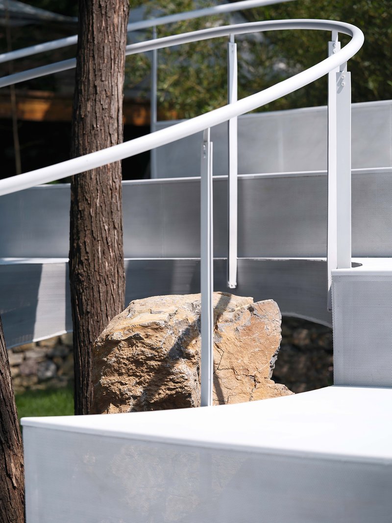 Detail of white tubular railing passing through a preserved boulder and tree trunk