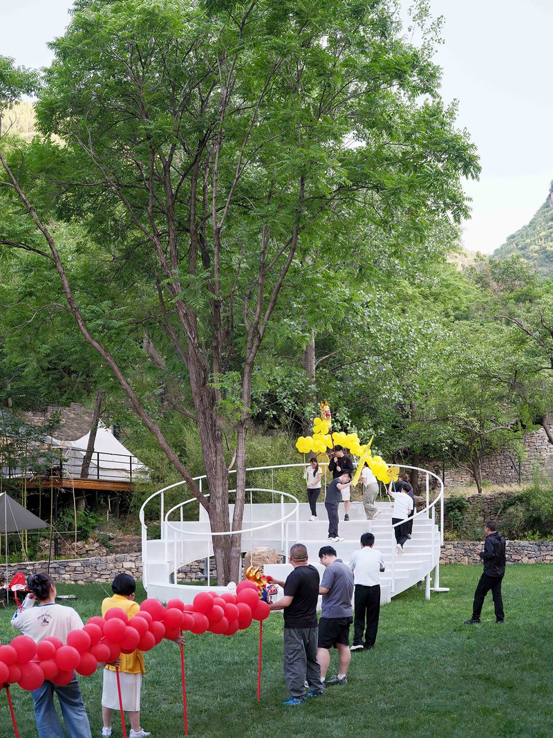 White spiral staircase winding around a tree in a lawn with visitors and red balloons