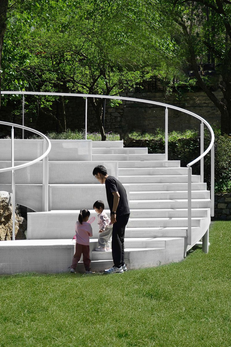Adult and two children standing on the white curved seating tiers in daylight